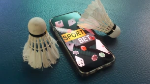 Smartphone with sport bet interface surrounded by badminton shuttlecocks and casino poker chips on a blue surface.